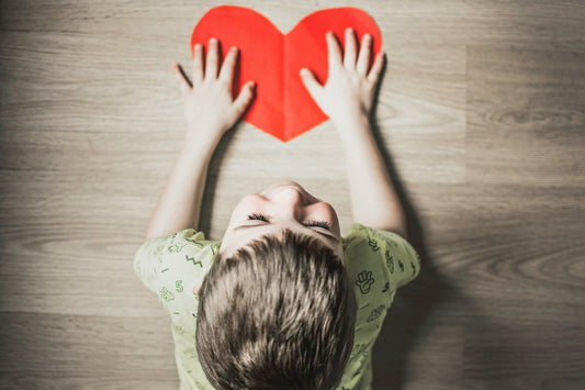 Child holding a red paper heart on the floor