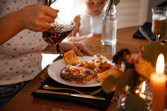 Parent pouring syrup on waffles while child watches at breakfast table