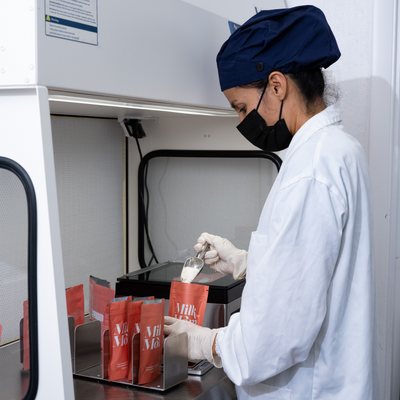 Lab technician wearing a mask and gloves carefully filling Milk by Mom packets with powdered breast milk inside a clean laboratory environment