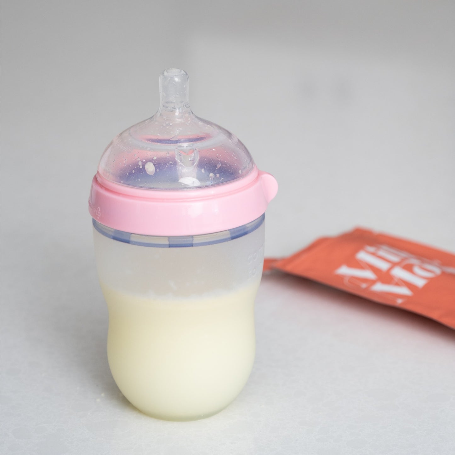 Baby bottle filled with reconstituted freeze-dried breast milk next to a Milk by Mom single-use pouch, showing convenient feeding with preserved breast milk powder
