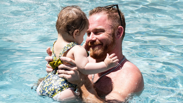 Smiling father holding his baby daughter in a swimming pool on a sunny day