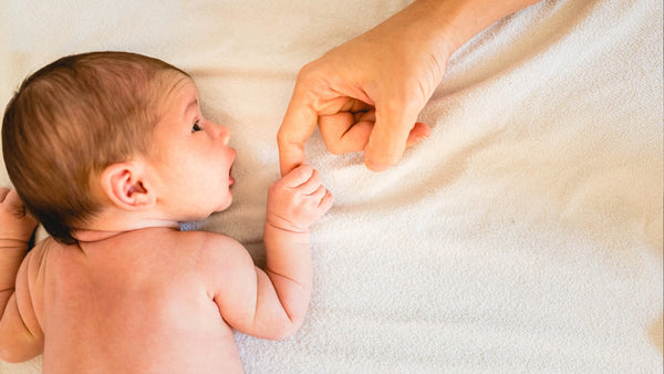 Newborn baby lying on a blanket holding an adult's finger