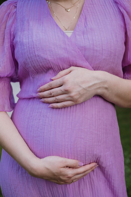 Pregnant woman holding her belly in a purple dress