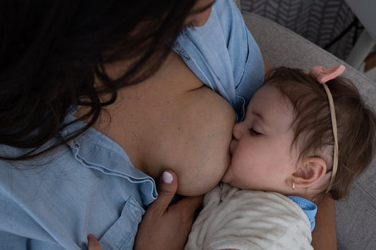 Baby with a headband breastfeeding while being held by their mother in a blue shirt