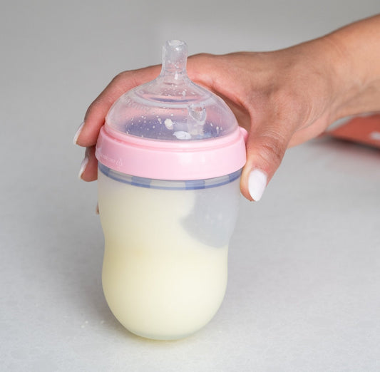 Hand holding baby bottle with pink lid and milk