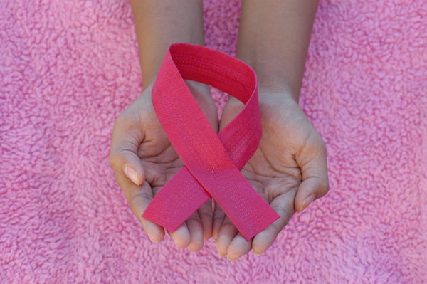 Hands holding a pink breast cancer awareness ribbon on a pink fabric background