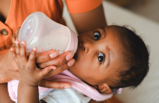 a baby drinking from a bottle looking up