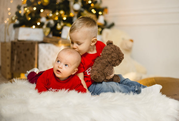 a toddler and baby boy under a christmas tree