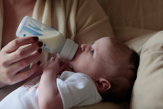 Baby drinking milk from a bottle while being hel