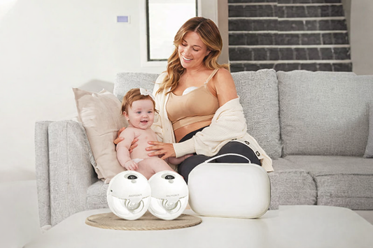 Mom sitting on a couch with her baby using a hands-free breast pump, showing modern breastfeeding, milk expression, and convenience for busy moms