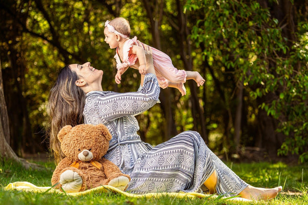 Mother lifting baby in the air outdoors in park, joyful bonding moment with infant and family lifestyle photography