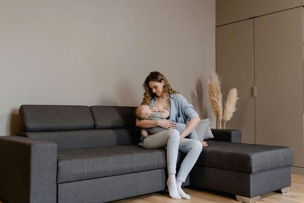 Mother breastfeeding baby on couch at home, comfortable nursing and bonding moment