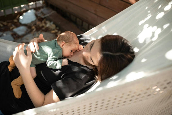 Mother relaxing outdoors while cuddling newborn, skin-to-skin bonding and breastfeeding lifestyle moment