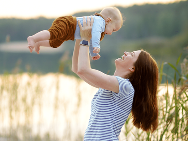 Mother lifting baby in the air by a lake at sunset, joyful bonding moment highlighting motherhood, infant care, and family connection