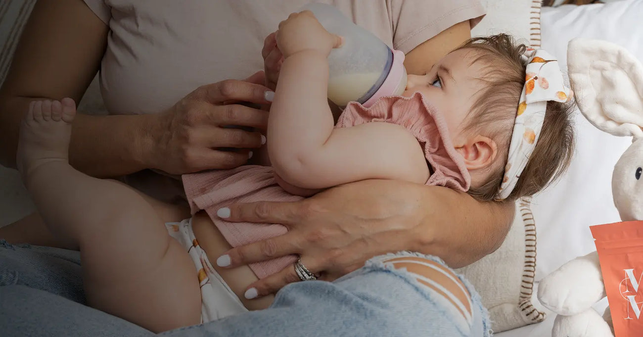 Mother feeding baby with a bottle of freeze-dried breast milk from Milk by Mom while cuddling on the couch