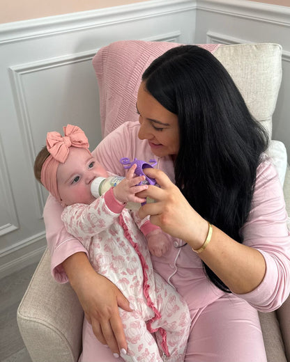 Mother sitting in a chair feeding her baby with a bottle while using a bottle toy attachment to keep the baby engaged during feeding time