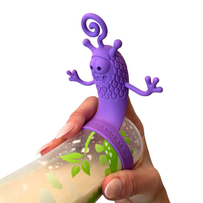 Hand holding a baby bottle filled with milk and topped with a purple silicone bottle toy attachment designed to keep babies entertained and focused during feeding