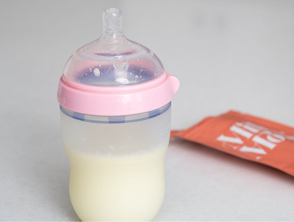 Baby bottle filled with rehydrated breast milk with a Milk by Mom pouch in the background, showcasing easy preparation, convenient feeding, and freeze-dried breast milk use