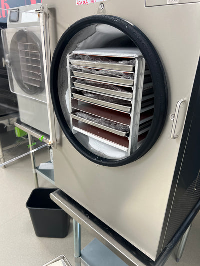 Open commercial freeze dryer showing multiple stainless-steel trays inside the processing chamber