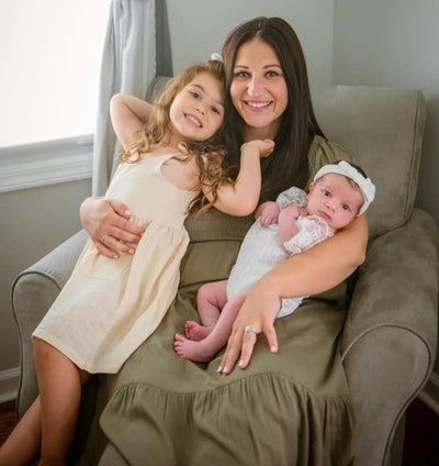 Mother holding newborn baby while young daughter cuddles beside her in a cozy home setting, heartwarming family moment celebrating motherhood and new baby bonding